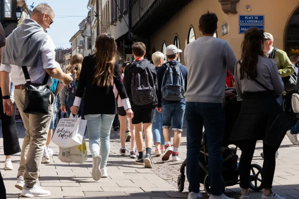 Groupe de passants déambulant dans une rue commerçante piétonne, devant la Place de la Cathédrale